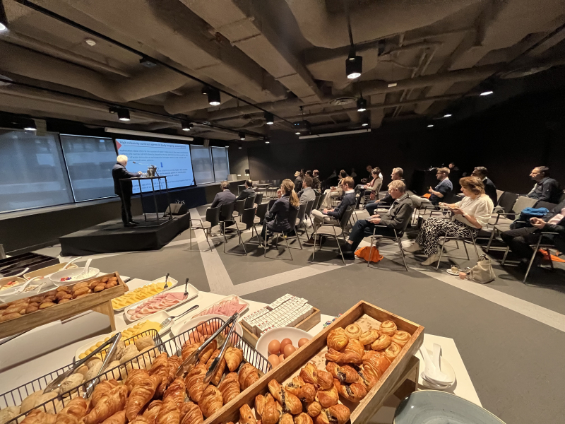 A speaker presents to an audience in a room with snacks.