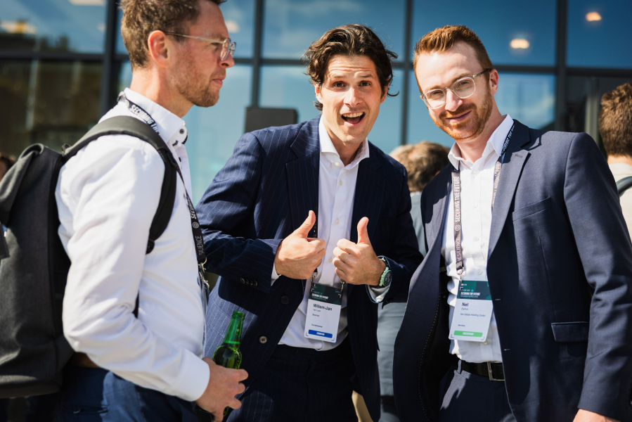 Three men happily posing in front of a building.