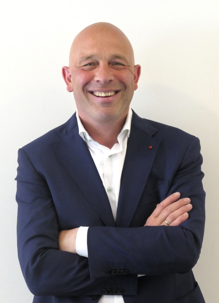 A man with a bald head and a blazer smiling warmly.