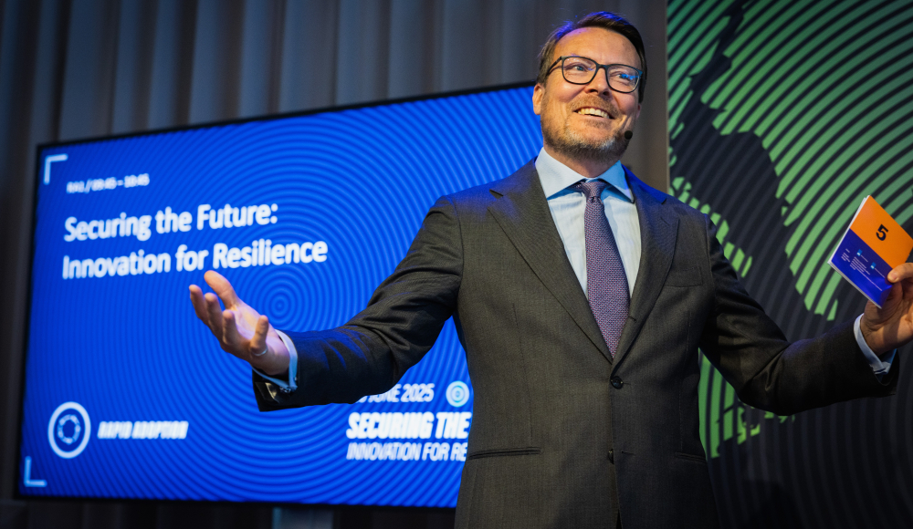 A man in a suit speaks enthusiastically at a conference.