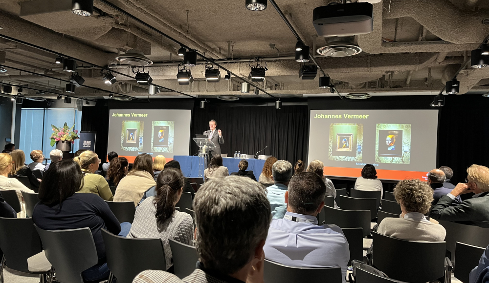 A speaker presents to an audience with images of Vermeer.
