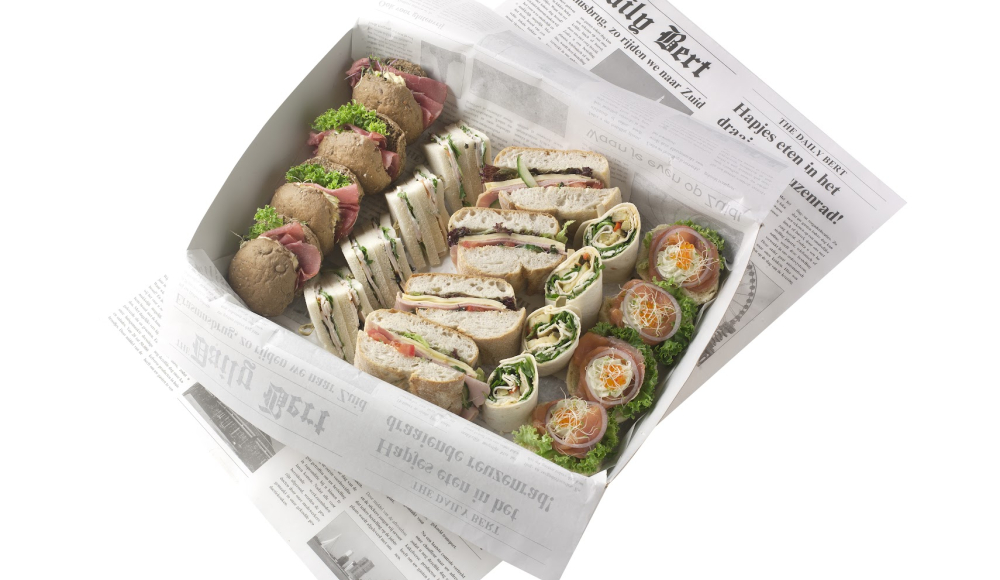 A box filled with assorted sandwiches and wraps on newspaper.
