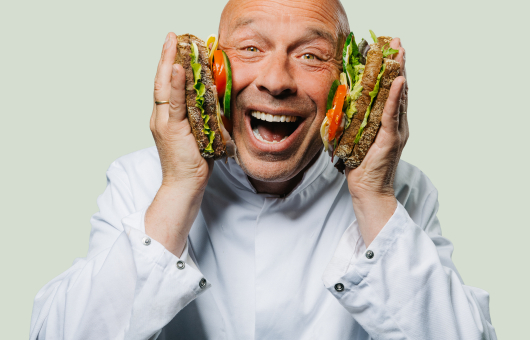 A man with a big smile holding two sandwiches.