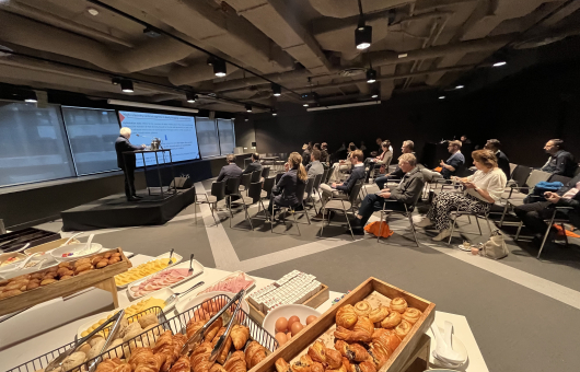A speaker presents to an audience in a room with snacks.