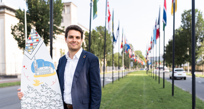 Image of international sales advisor Joris holding branded surfboard of The Hague in the International Zone of The Hague