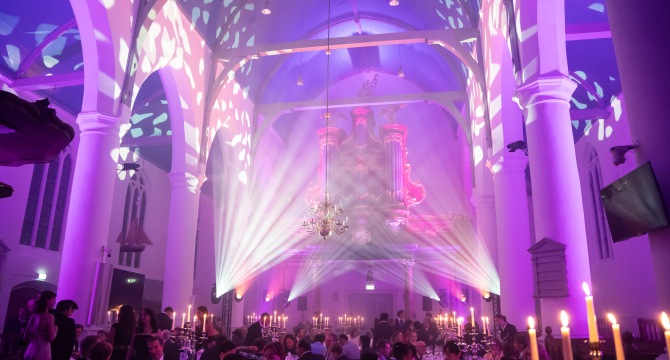 Interior of a hall with a light show and guests at dinner tables.