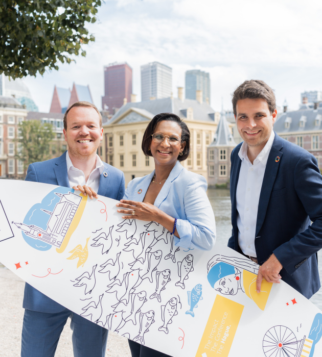 Image of three people of The Hague and Partners holding a branded surfboard standing in front of the Hofvijver in The Hague