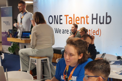 A child sits at a table with an adult, looking at a laptop.