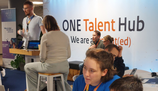 A child sits at a table with an adult, looking at a laptop.
