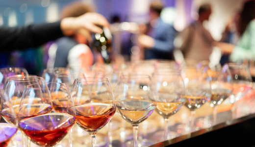 Row of various wine and water glasses with a hand pouring from a bottle