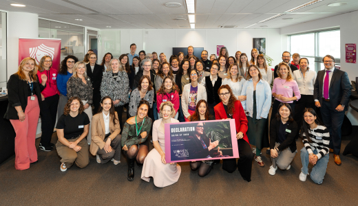 A large group of women poses together with a sign for the camera.