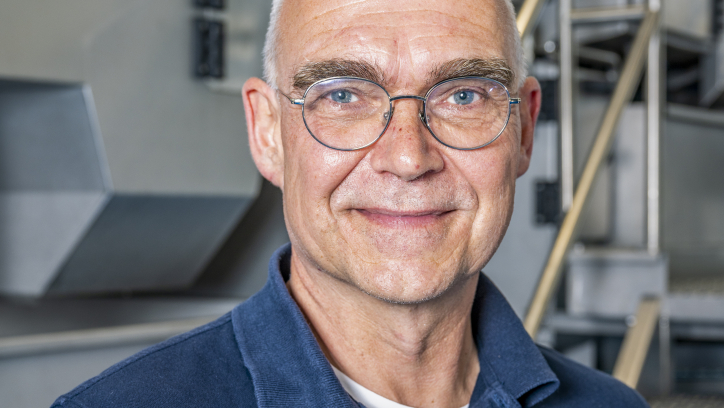 Een man met bril poseert in een werkplaats.