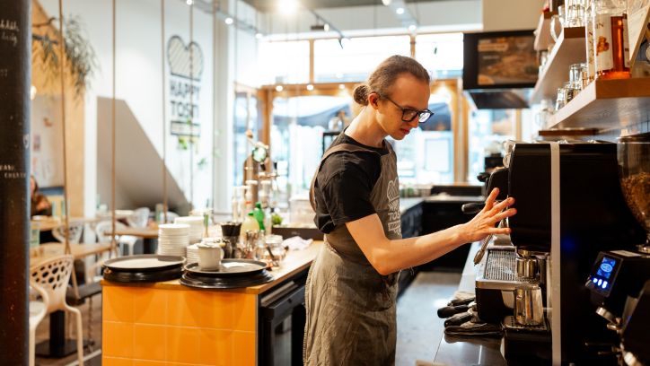 Een jonge man in een schort bedient een koffiezetapparaat in een modern café.