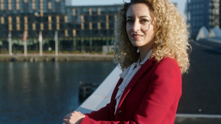 Vrouw met krullend haar in een rode blazer bij het water.