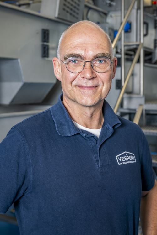 Een man met bril poseert in een werkplaats.