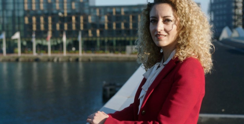 Vrouw met krullend haar in een rode blazer bij het water.