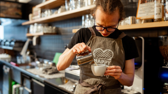 Een barista giet melk in een wit koffiekopje in een café.