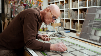 Een man werkt met glas-in-lood aan een tafel.