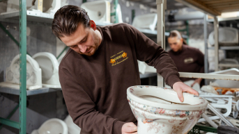 Een man houdt een ornamentale toiletpot vast in een werkplaats.