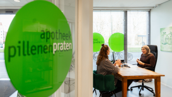Twee vrouwen in gesprek in een apotheek.