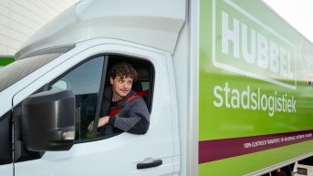 Jongeman met krullen zit in een elektrische vrachtwagen.