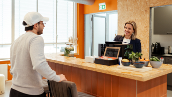 Een man in een grijs sweatshirt praat met een vrouw achter de bar.