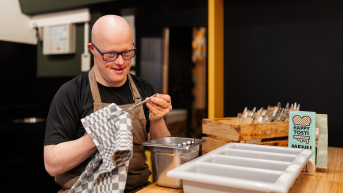 Man met een bril en schort, bezig met koken