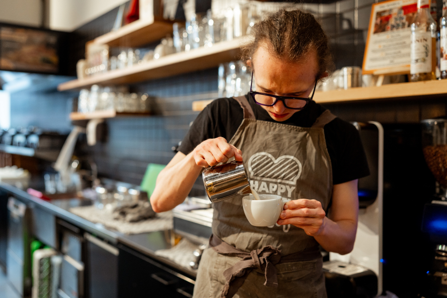 Een barista giet melk in een wit koffiekopje in een café.