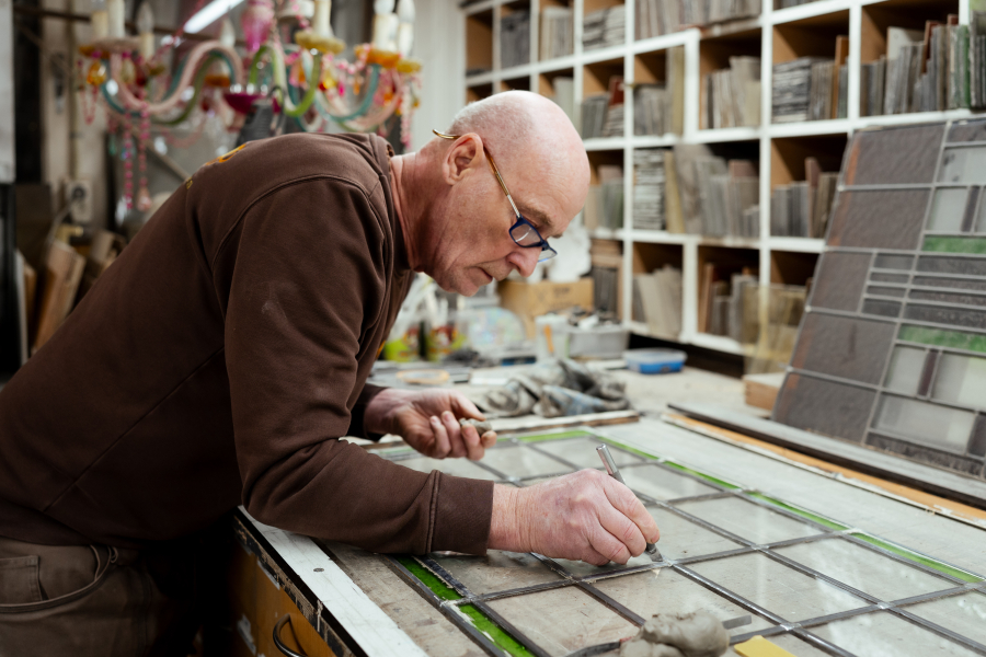 Een man werkt met glas-in-lood aan een tafel.