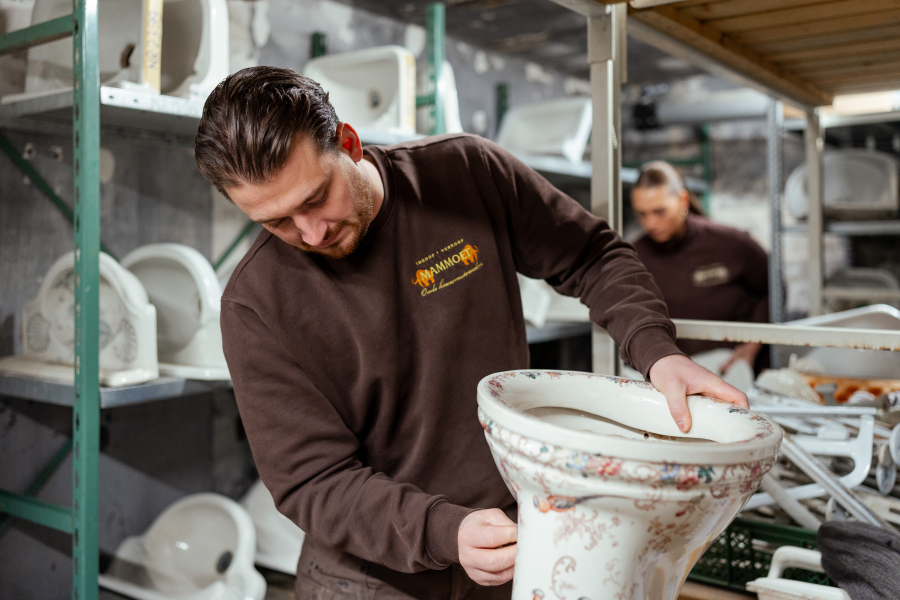 Een man houdt een ornamentale toiletpot vast in een werkplaats.