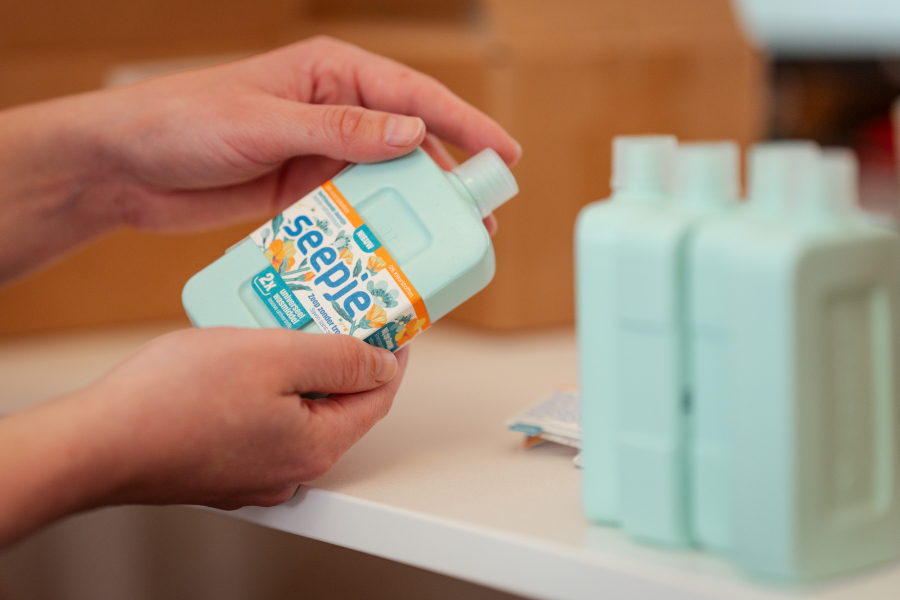 Een hand houdt een flesje zeep met een etiket vast.