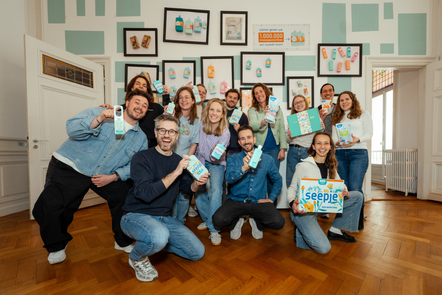 Een diverse groep mensen poseert met melkproducten in een kamer.