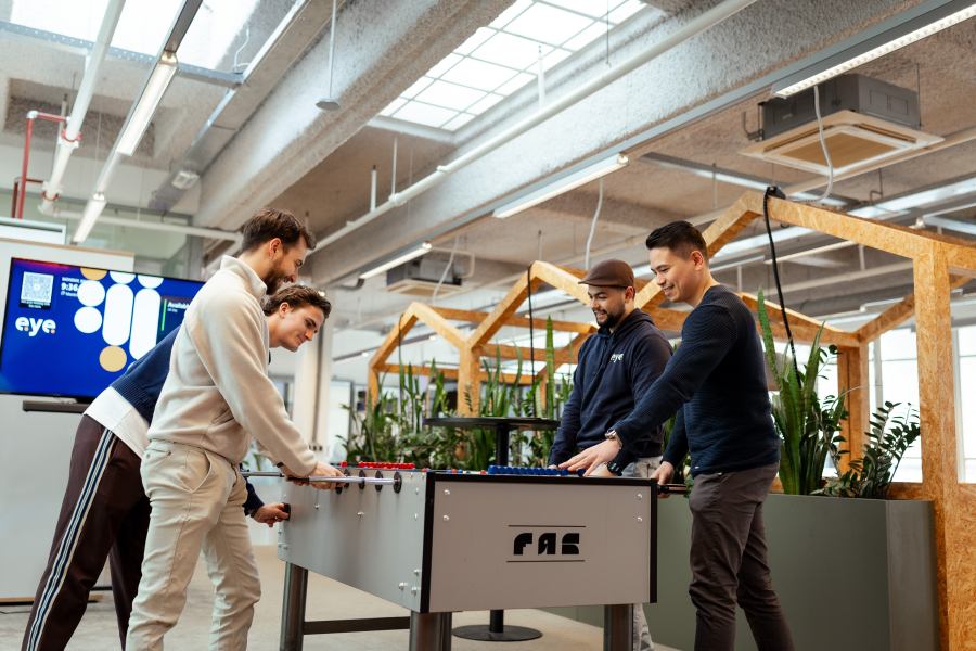 Drie mensen spelen tafelvoetbal in een moderne ruimte.