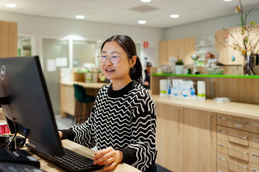 Een vrouw met een zwart-wit trui glimlacht achter een computer.