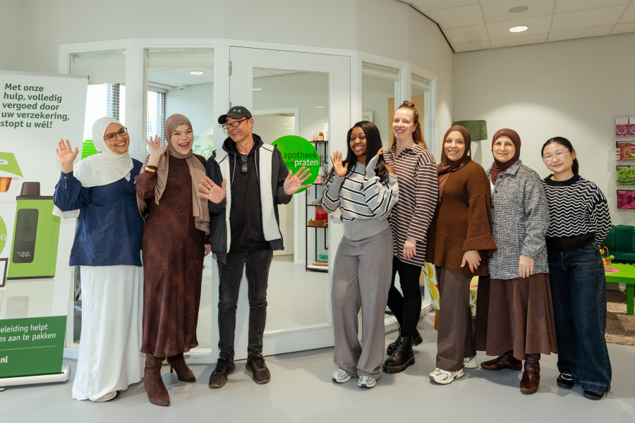 Acht mensen staan lachend voor een apotheekinterieur.