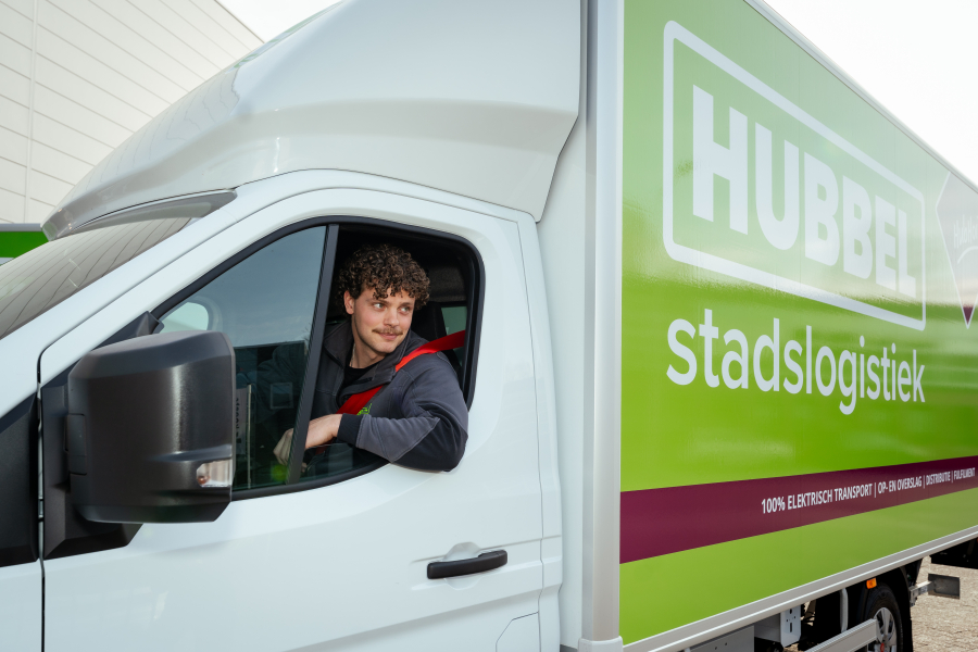 Jongeman met krullen zit in een elektrische vrachtwagen.