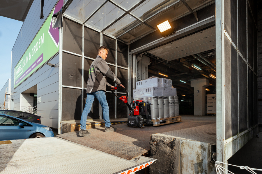 Een man rijdt een pallet met flessen uit een magazijn.