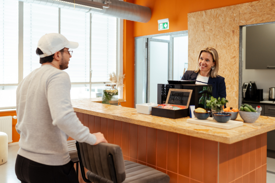Een man in een grijs sweatshirt praat met een vrouw achter de bar.