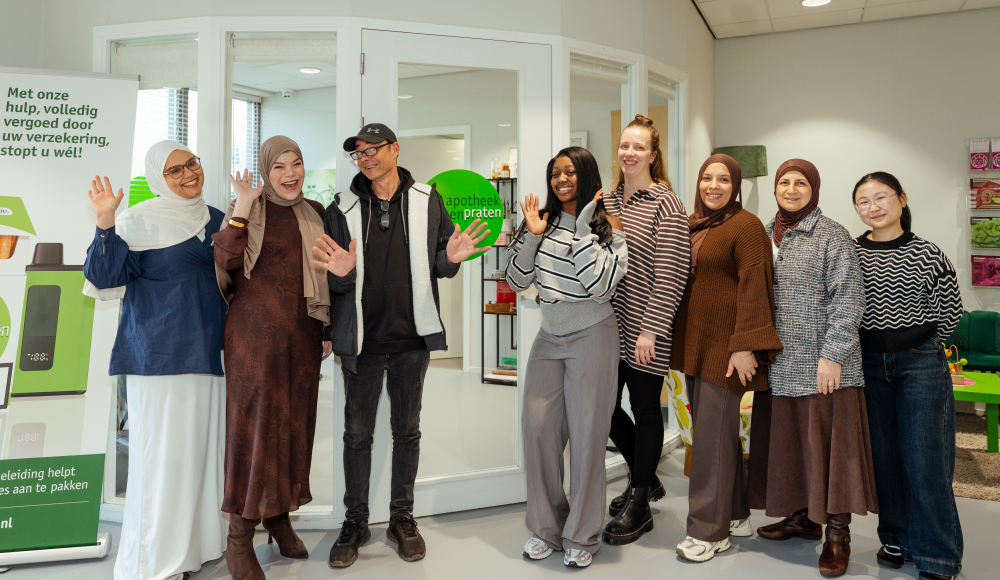 Acht mensen staan lachend voor een apotheekinterieur.