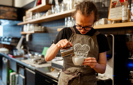 Een barista giet melk in een wit koffiekopje in een café.