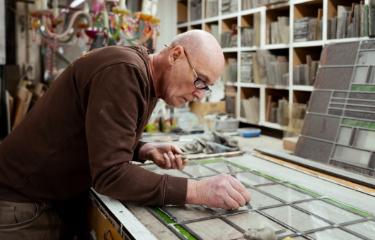 Een man werkt met glas-in-lood aan een tafel.