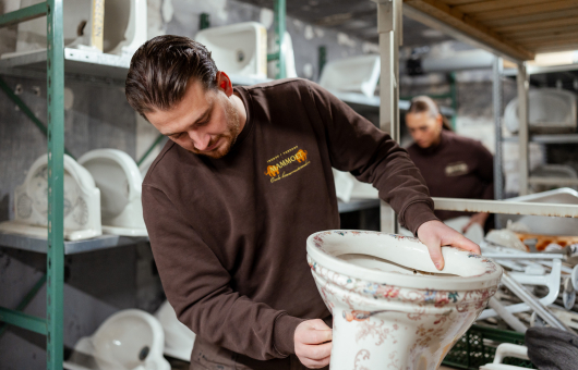 Een man houdt een ornamentale toiletpot vast in een werkplaats.
