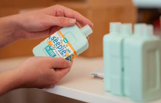 Een hand houdt een flesje zeep met een etiket vast.