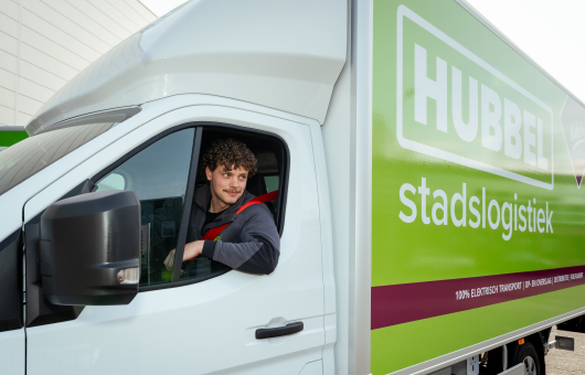 Jongeman met krullen zit in een elektrische vrachtwagen.