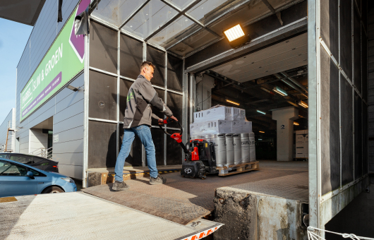 Een man rijdt een pallet met flessen uit een magazijn.