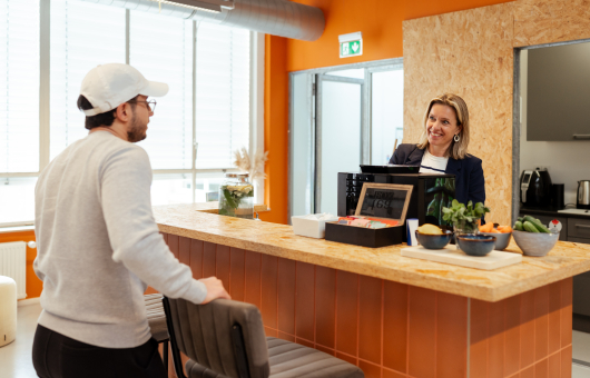 Een man in een grijs sweatshirt praat met een vrouw achter de bar.