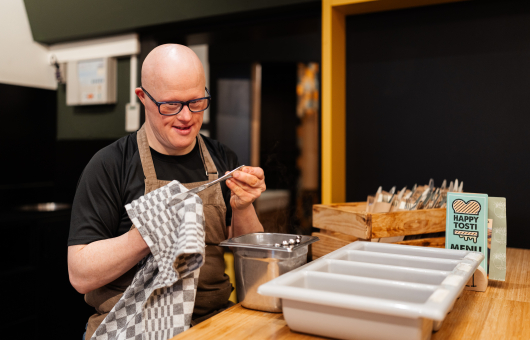 Man met een bril en schort, bezig met koken