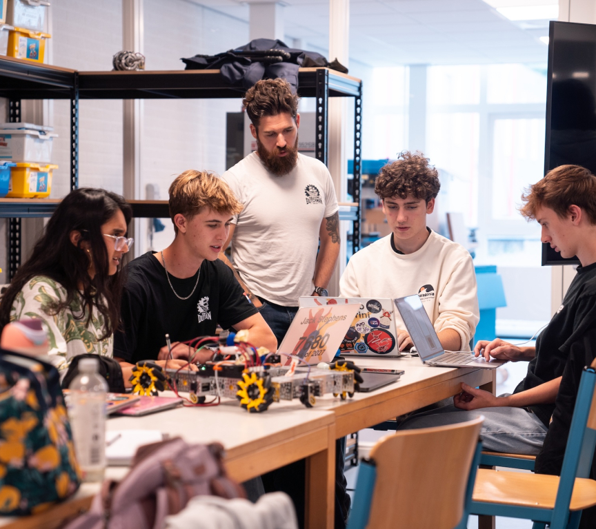 A group of high school students working on a robot with their coach.