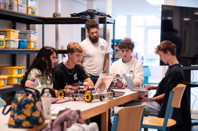 A group of high school students working on a robot with their coach.