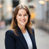 Woman with long brown hair, smiling in business outfit.